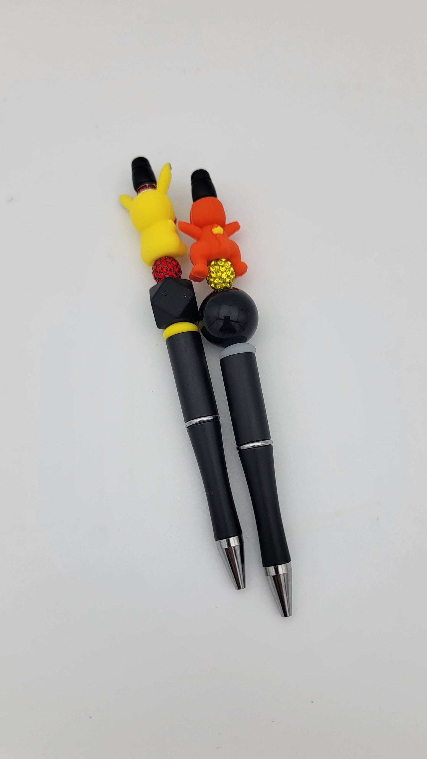 A pair of black Beaded Pens from the 2 in 1 bag set features colorful cartoon character toppers and decorative beads on a plain white background.