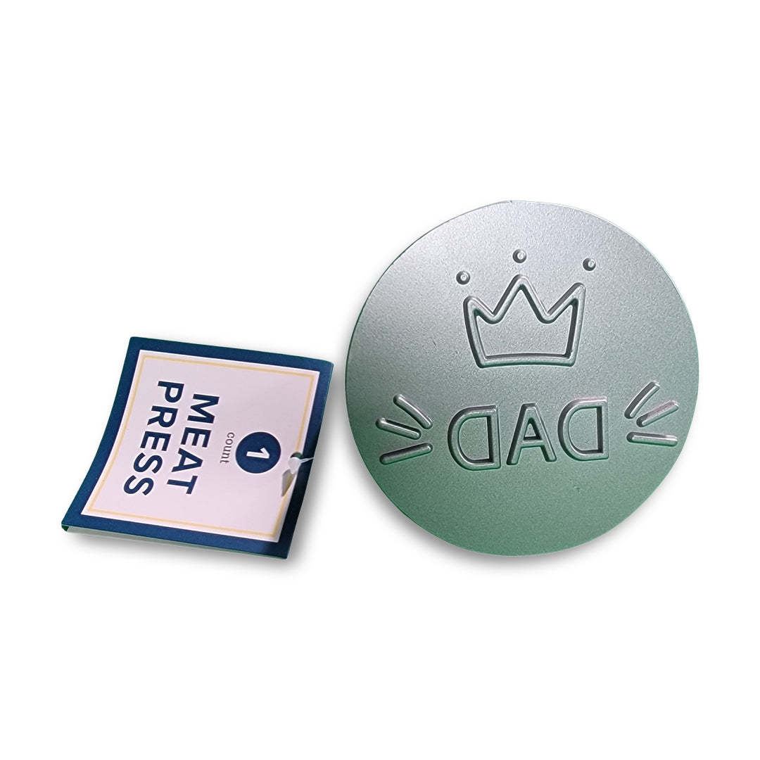Round metal Meat Press-Dad featuring a crown design, accompanied by a small "MEAT PRESS" instruction booklet.