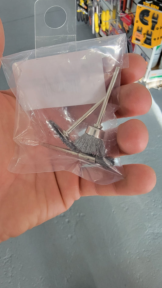 A hand holds a transparent plastic bag containing two Mini T-shaped Steel Wire Brass Brushes for a drill.