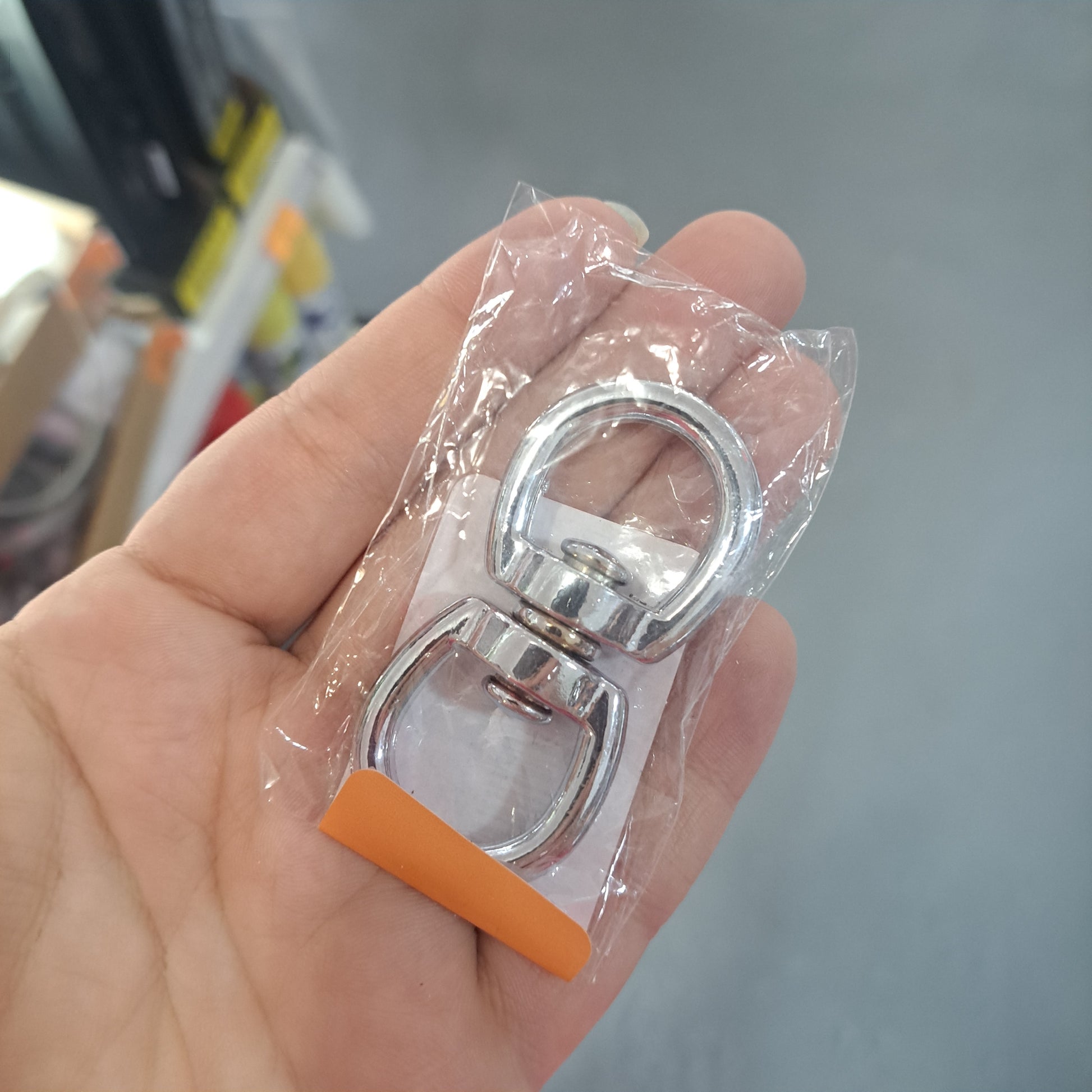 Individual holding a packaged 5/8" double swivel metal snap hook in their hand.