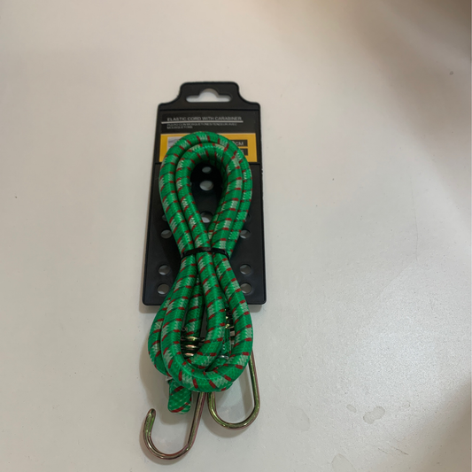 A green bungee cord with red accents and metal hooks is placed on black packaging featuring a yellow and black label, resting on a white surface. Product: Bungie cord w carabiner.