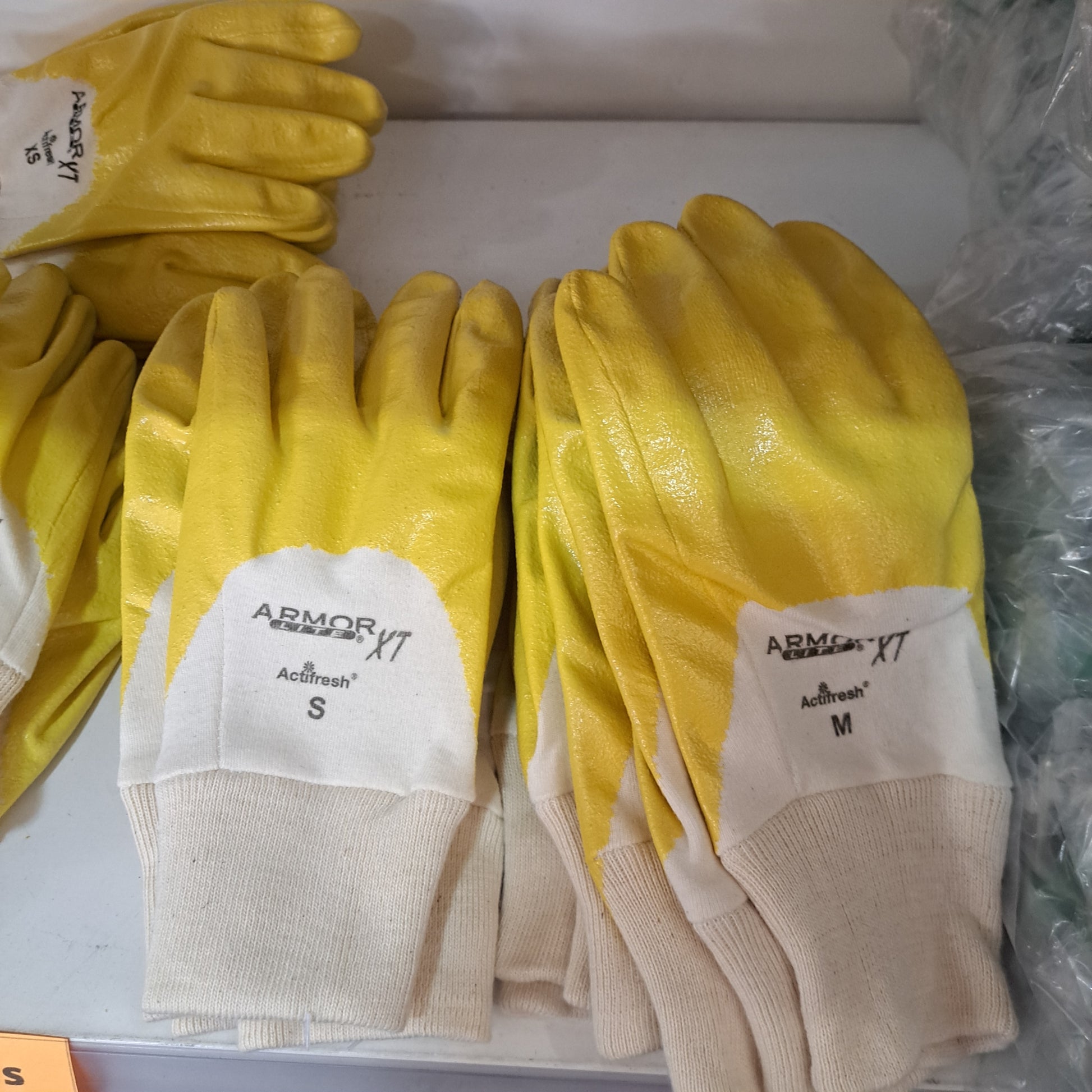 Yellow and white Armor yellow gloves in sizes S and M arranged on a shelf.