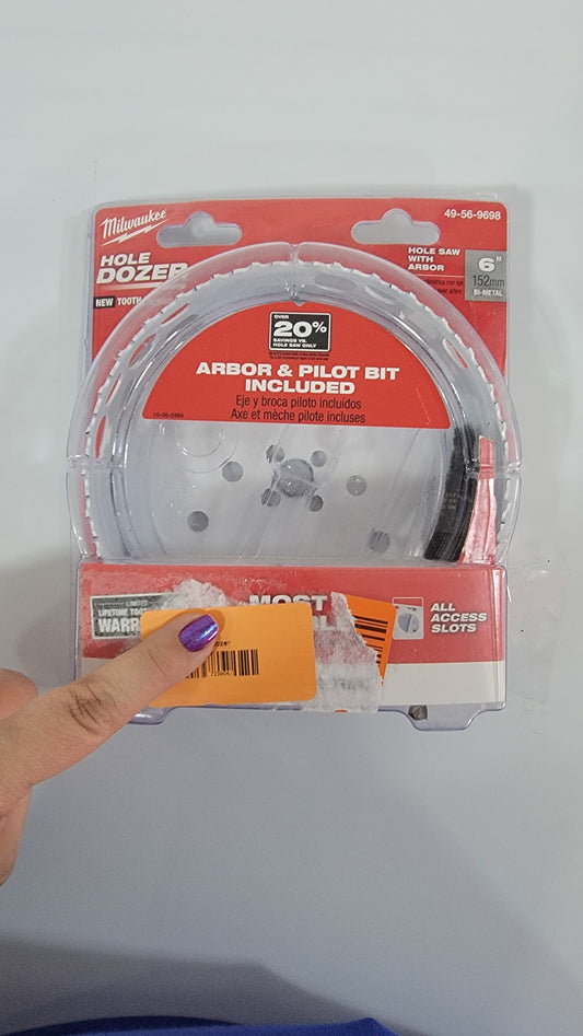 A person holding a packaged 6" Hole Dozer. The packaging is red and white, branded "Milwaukee Hole Dozer," featuring an arbor and pilot bit included.