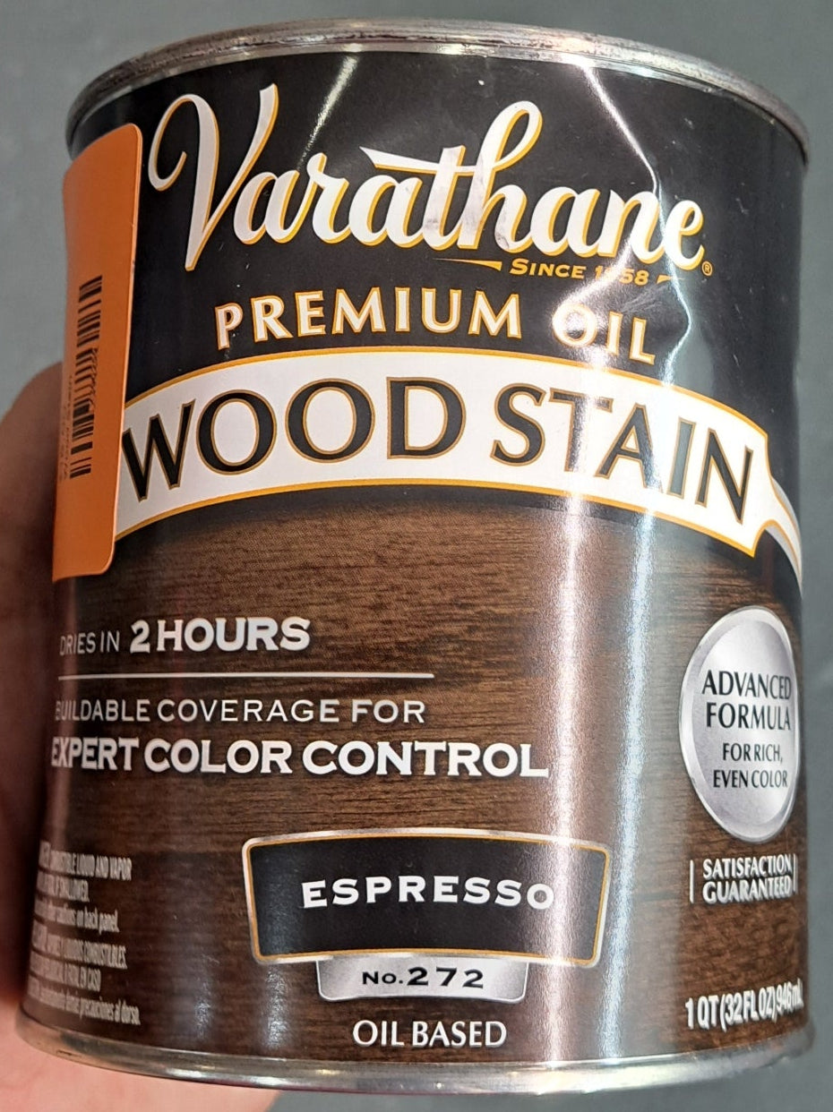 A hand holds a can of Wood Stain, labeled "Espresso," against a gray background.